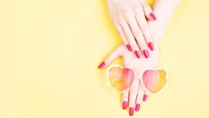 Summer manicure background. Beautiful female hands with perfect vibrant nails on yellow background. Heart shape sunglasses. Hands and nails care concept. Flat-lay, top view. Copy space.