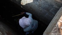 Seorang pekerja menyusuri got untuk mengukur lebar, dalam, dan tinggi saluran air yang diperbaiki.