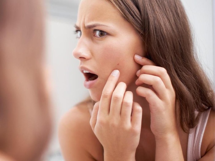 637875082 Cropped shot of a young woman squeezing a pimple on her face