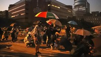 Mengenakan jas hujan, masker, dan payung, para pengunjuk rasa menghambur menghindari tembakan gas air mata dan water cannon. Kin Cheung/AP Photo.