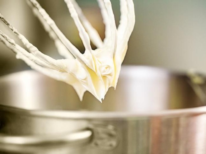 Young woman in kitchen using mixer for wiped cream