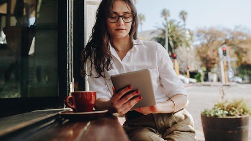 Woman sitting at a cafe working on digital tablet. Businesswoman sitting at cafe counter with a coffee using tablet computer.