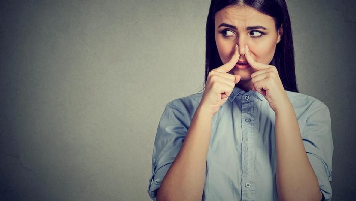 Woman pinches nose with fingers looks with disgust away something stinks bad smell isolated on gray background.