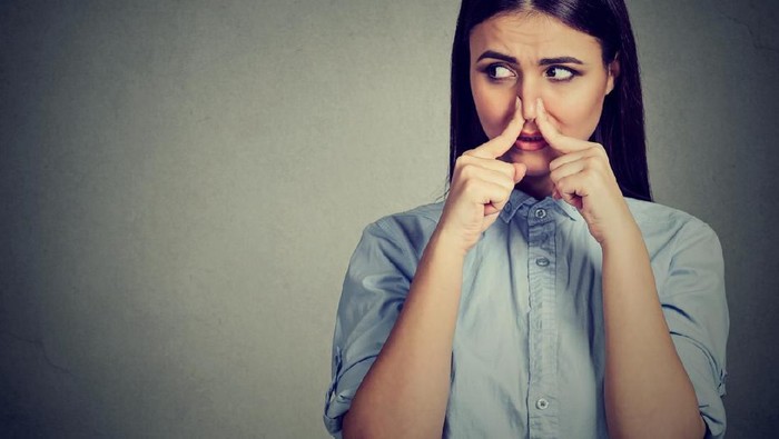 bau ketiak Woman pinches nose with fingers looks with disgust away something stinks bad smell isolated on gray background.