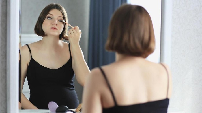 ibu hamil dandan Young beautiful woman is doing makeup and looking in the mirror. She has got full lips, big blue eyes, blonde hair, white skin