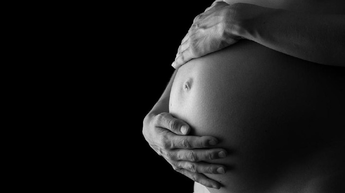 Greyscale image of woman tenderly holding her pregnant belly attentively turning to her unborn child.