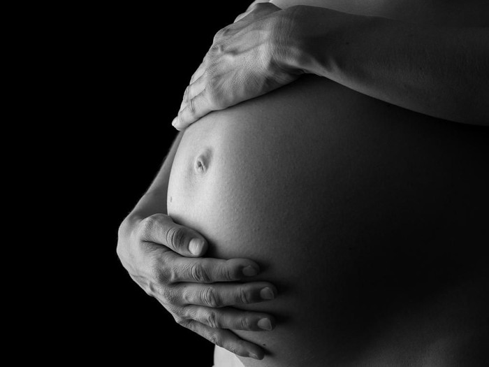 Greyscale image of woman tenderly holding her pregnant belly attentively turning to her unborn child.