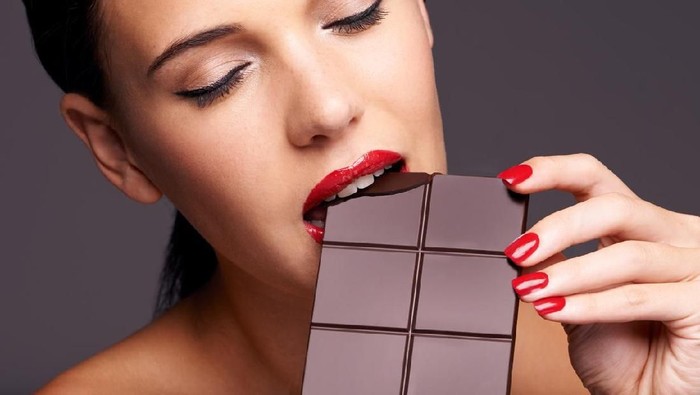 514321189 Closeup portrait of a cute young female biting into a piece of chocolate