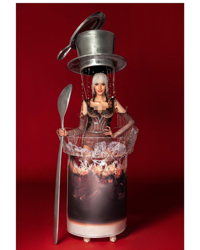 Mia Hong tampil memakai teko kopi Vietnam ukuran raksasa di atas kepalanya. Dia juga memegang sendok raksasa. Sedangkan busana, Mia mengenakan jumpsuit bertabur bebatuan kristal yang berkilauan. Rambutnya memakai wig ala Cleopatra.  Foto: Instagram @missuniversevietnam, @hoangthuy_official