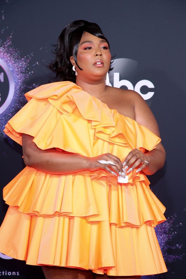 Pelantun Truth Hurts itu muncul dalam balutan gaun mini Valentino dengan garis leher asimetris. Gaun oranye tersebut hadir dengan gaya ruffle bertumpuk.  (Foto: Getty Images)