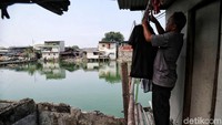 Seorang warga menjemur pakaian di depan rumah yang dibangun di atas air.