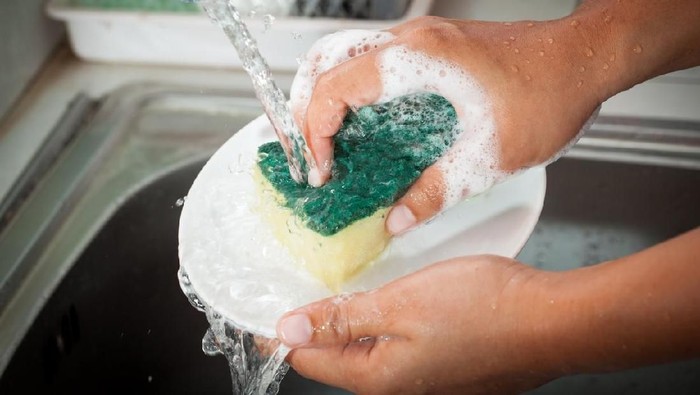 Woman hand washing dishes over the sink in the kitchen