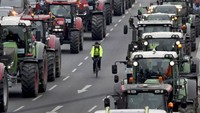 Seorang warga melintas menggunakan sepeda di antara deretan traktor milik para petani yang terparkir di dekat Gerbang Brandenburg, Berlin, Jerman. Michael Sohn/AP Photo.