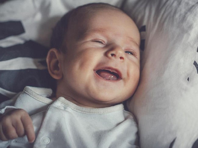 Sleeping, nine day old, newborn baby boy with a smile on his face. He is swaddled in a light blue wrap. Shot in the studio on a white, sheepskin rug.