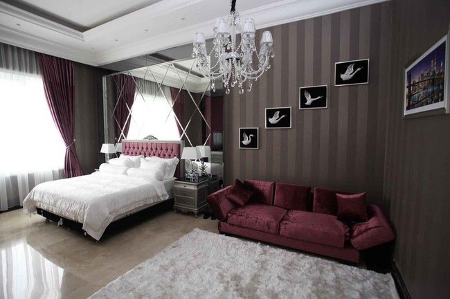Inilah kamar tidur Nikita Willy yang mewahnya bak hotel. Tampak lampu kristal chandelier menggantung di kamar tidur yang dihiasi wallpaper cokelat bergaris ini. Nikita juga menerapkan kaca pada bagian tempat tidurnya sehingga menambah kesan luas pada area kamar yang diberikan sentuhan warna merah melalui sofa dan sandaran tempat tidur. Foto: Instagram, YouTube