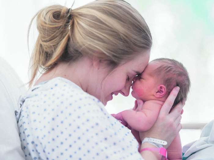 melahirkan A mother is touching foreheads with her newborn daughter. They are laying in a hospital bed.