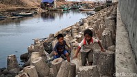 Dua orang anak bermain di atas beton pemecah ombak yang berada di seberang proyek pembangunan jalan.