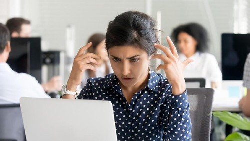 Upset indian female worker sitting at desk in office looking at pc screen feels unhappy and shocked. Millennial hindu woman reading unpleasant notification having system fault and big troubles concept