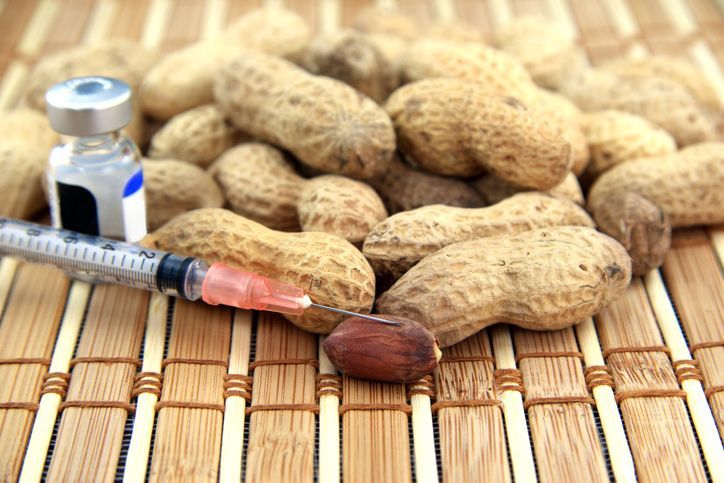 Many peanuts with a syringe and a bottle of medication for allergy on a wood tablecloth