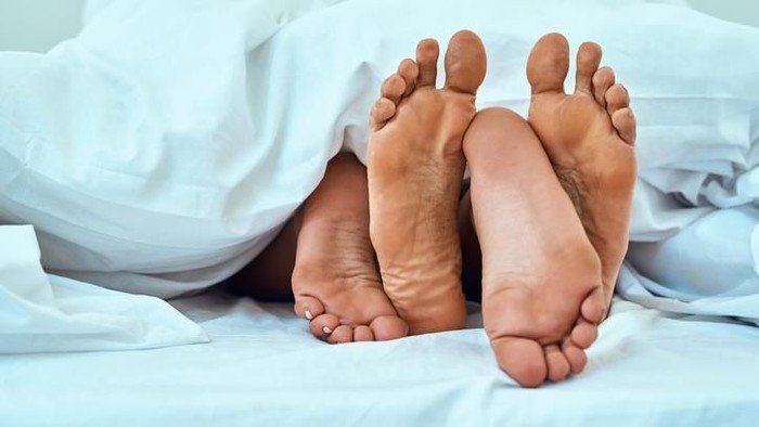 Shot of a coupleâ€™s feet poking out from under the bed sheets