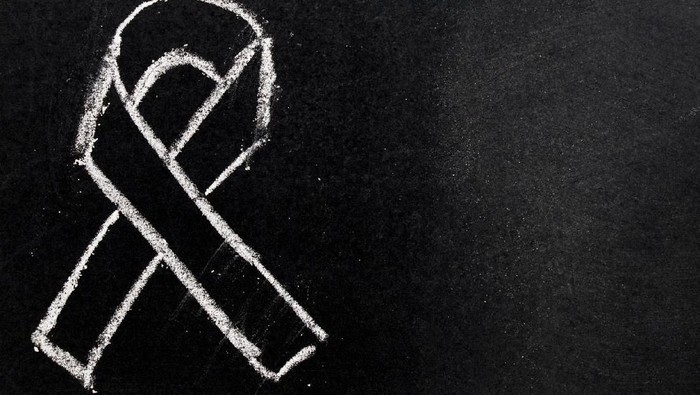 Hand holding black ribbon on black background mourning awareness sign