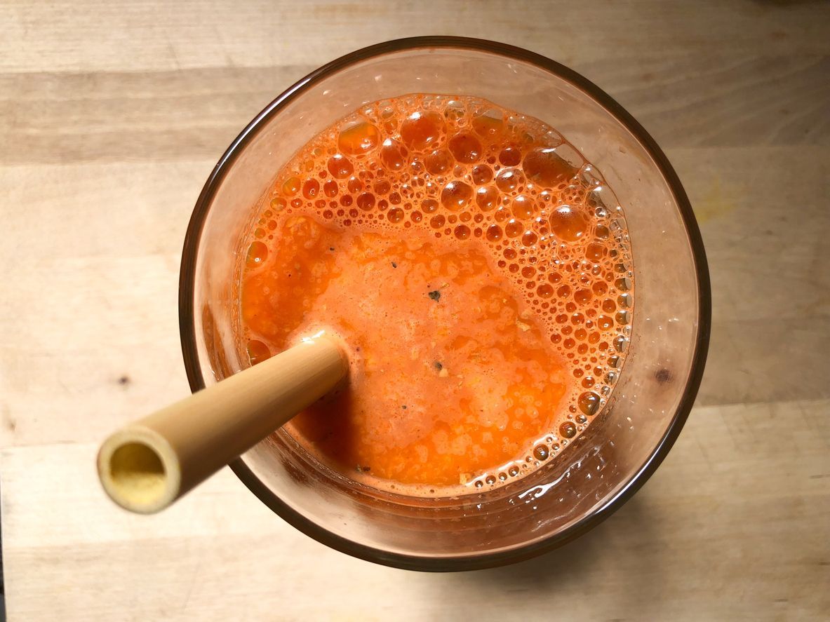 Healthy glass of fresh organic carrot apple juice with turmeric, black pepper, and a dash of cayenne powder with a natural bamboo straw on a kitchen cutting board
