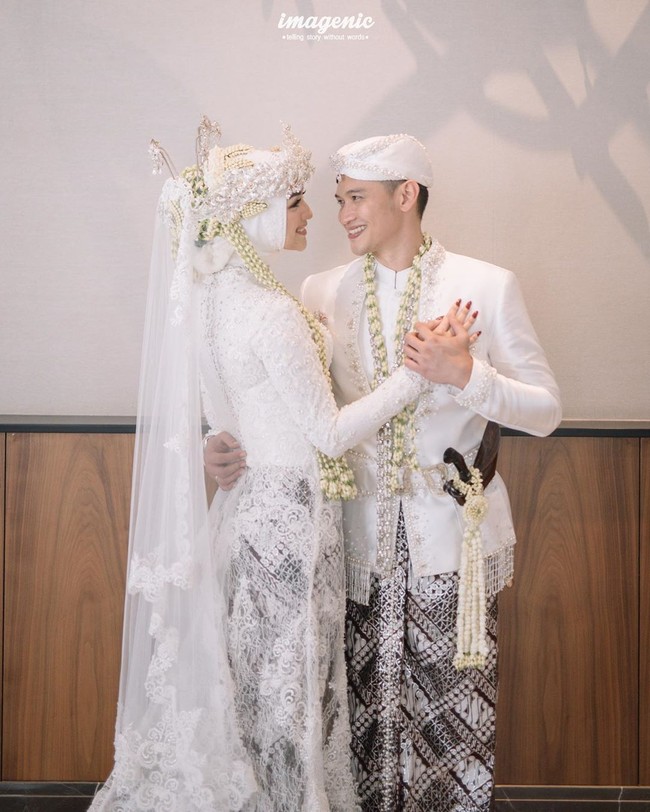 Sejoli pengantin baru Citra Kirana dan Rezky Aditya berpose dalam balutan busana pengantin Sunda. Citra Kirana, terlihat dibalut kebaya lace warna putih dengan train panjang menyapu lantai. Sementara itu kainnya menggunakan batik klasik bernuasana cokelat. Dan Rezky mengenakan beskap berpotongan slimfit ditambah kain batik yang sama dengan istrinya. Foto: Dok. Imagenic Wedding Photography