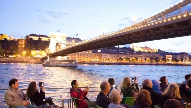 People sitting in a cruise boat on the Danube river and passing under Chain Bridge at summer night