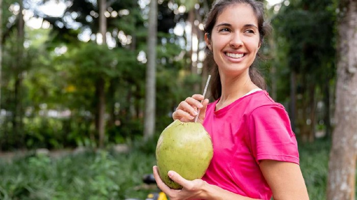 Air kelapa Happy Brazilian woman drinking coconut water after training at the park - healthy lifestyle concepts