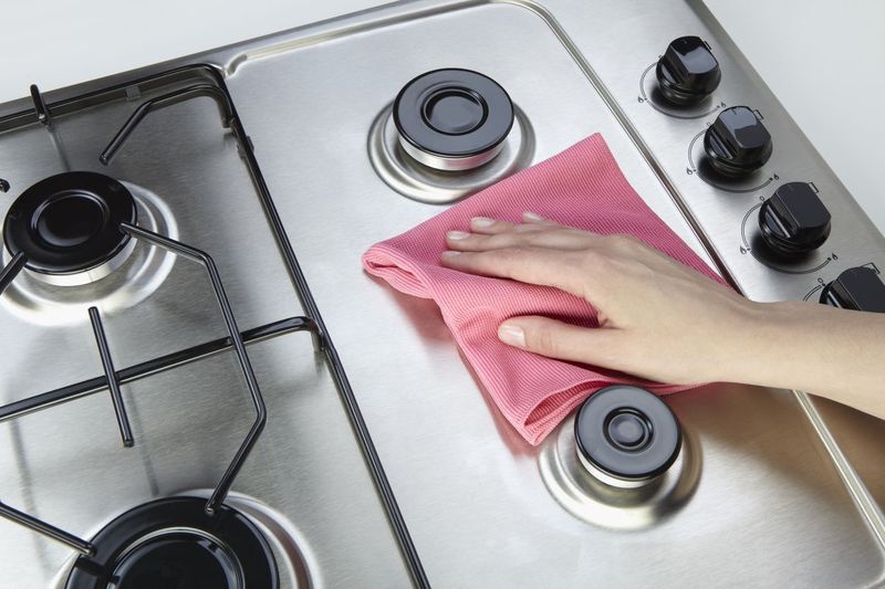 young woman in protective glove with rag cleaning stove. Girl polishing kitchen. People, housework, housekeeping, cleaning concept