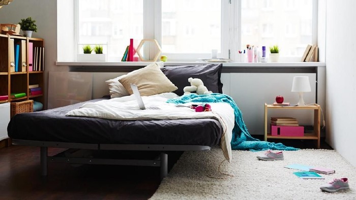 Modern messy girl bedroom with large bed, laptop, teddy bear and scattered sneakers on white soft carpet