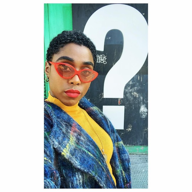 Lashana Lynch juga memaksimalkan gayanya dengan aksesori unik nan plyaful. Salah satunya kacamata oranye bergaya cat-eye ini. (Foto: Instagram/@lashanalynch)