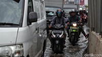 Seorang pengendara mengangkat kakinya guna menghindari banjir saat melintasi jalan di kawasan Boulevard Kelapa Gading, Jakarta Utara.