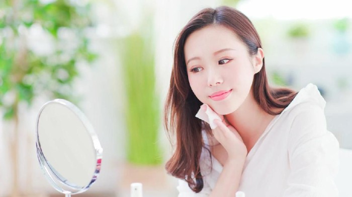 Smile asian woman remove makeup by Cleansing Cotton and look mirror at home