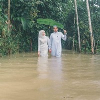 Pasangan di Thailand Selatan mencuri perhatian setelah memutuskan untuk tak membiarkan cuaca meredam perayaan istimewa pernikahan mereka. Meskipun harus berjibaku dengan air banjir pasangan pengantin ini tetap bahagia. Foto: Facebook Meen Photographer