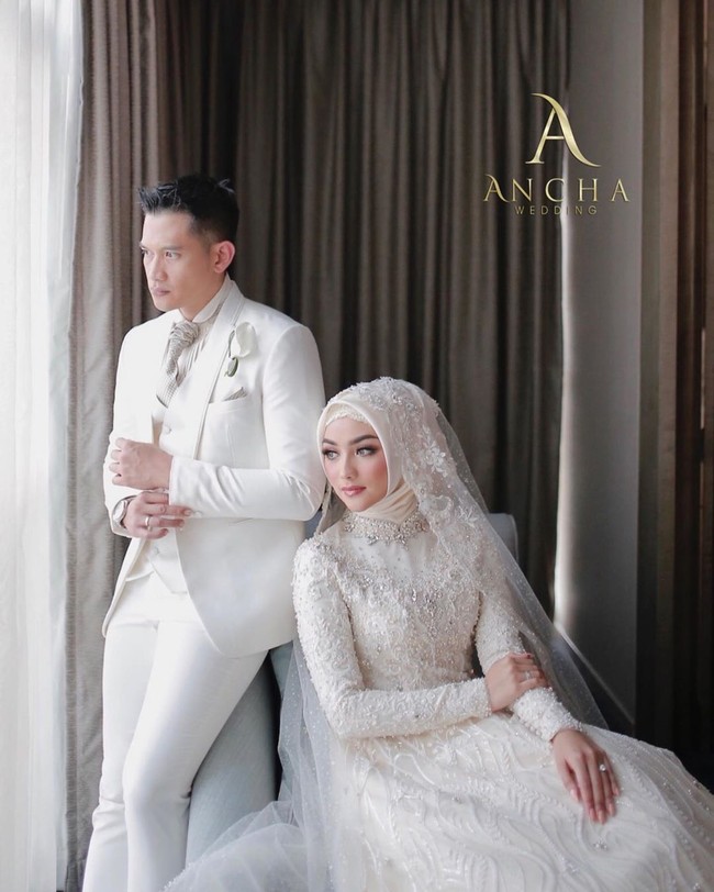 Sementara itu, Rezky Aditya juga tak kalah modis. Senada dengan warna gaun istrinya, sang aktor mengandalkan setelan putih. Sebagai pemanis, sekuntum bunga Calla Lily disematkan di dekat kantong sebagai pengganti korsase yang elegan. (Foto: Instagram/@anchawedding)