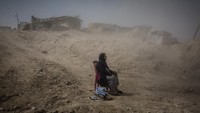 Nadhira Aziz terlihat duduk sambil melihat pengemudi excavator yang tengah menggali puing-puing rumahnya dari serangan udara. Ia memastikan bahwa jenazah saudara perempuan dan keponakannya yang terbunuh bisa ditemukan pada 16 September 2017.