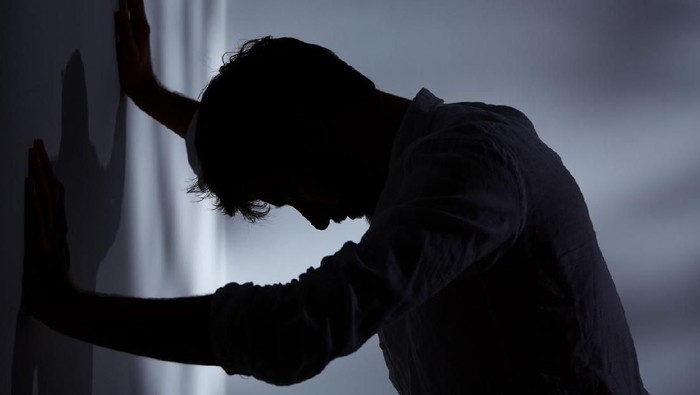 Man leaning with hands against wall, dark room