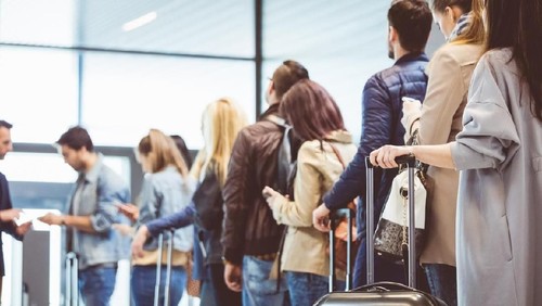 Mother picking backpack from security counter while standing by daughters. Family is with luggage at airport terminal. They are going on vacation.