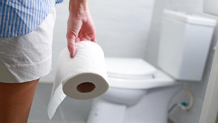 Woman holds toilet paper roll in front of toilet bowl.