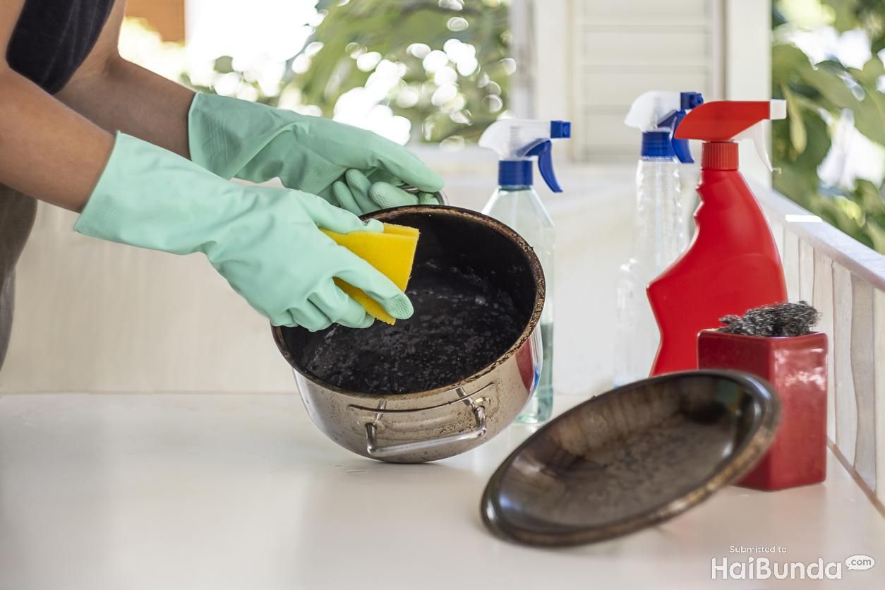Woman trying to clean burnt pan with chemical cleaners.