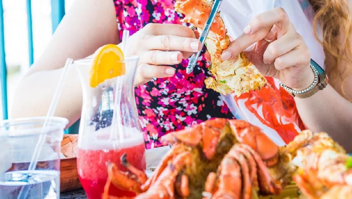 Closeup of lobsters and seafood on plate with woman shucking or shelling crab leg with hands on platter
