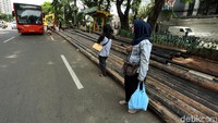Warga terpaksa menunggu bus di badan jalan karena halte terhalang pipa kabel.