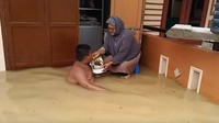 Rumahnya dikepung banjir. Namun, bocah ini asyik berenang. Sambil berenang, ia juga disuapi makanan oleh neneknya. Seru banget ya? Foto: Istimewa