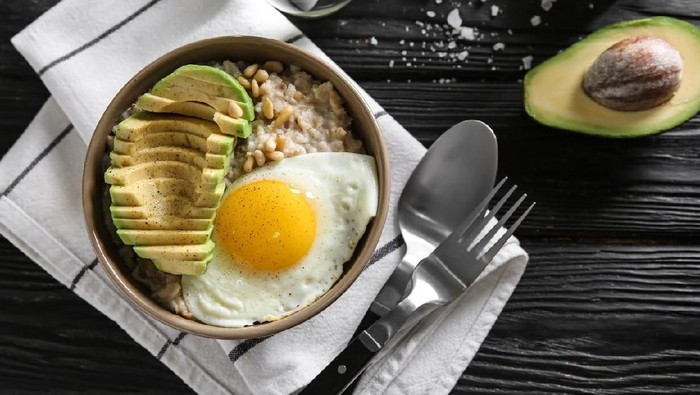 1139821615 Bowl with delicious oatmeal, egg and avocado on wooden table