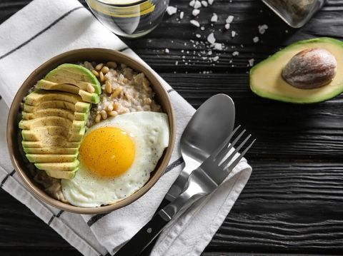 Bowl with delicious oatmeal, egg and avocado on wooden table