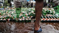 Seorang petugas tengah membuang miras dari dalam botol sebelum digilas dengan alat berat.