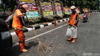 Dua orang petugas membersihkan bunga yang mengotori pinggir jalan di depan Gedung KPK.