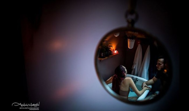 Rasa sakit karena kontraksi bisa diredakan dengan sejumlah cara. Potret karya Ashley Marston Photography ini menampilkan momen ibu menenangkan rasa sakit kontraksinya dengan berendam di dalam bathtub dengan didampingi sang suami. Foto: Dok. Ashley Marston Photography