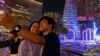Dua orang pengunjung berfoto bersama dengan latar pohon Natal raksasa yang nampak berkilau dengan hiasan lampunya di saat malam.